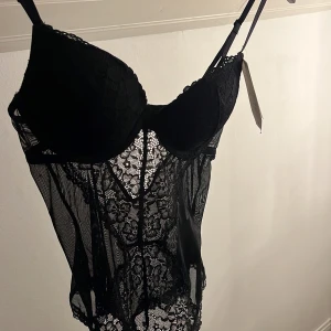 Svart spetsbody från H&M, 75A - Säljer en svart body från H&M med blommig spets och meshdetaljer. Toppen har vadderade kupor och justerbara axelband. Perfekt för dig som vill ha en statement piece med genomskinliga partier och vacker spets.