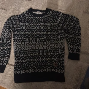 Svartvit stickad tröja XS - Säljer en svart stickad tröja i storlek XS med vitt nordiskt mönster över hela tröjan. Rund hals och långa ärmar, perfekt för kalla dagar. Tröjan har en snygg detalj med märke nedtill. Passar dig som gillar klassisk vinterstil. Köpt för 1700 i Norge 