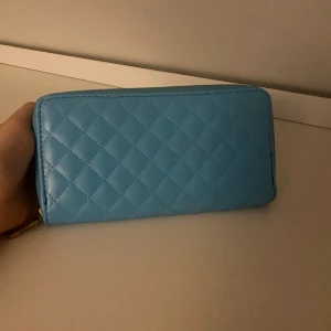 Blå quiltad plånbok med dragkedja - Snygg blå plånbok med quiltat mönster och guldfärgad dragkedja. Insidan har flera fack för kort och mynt, perfekt för att hålla ordning på allt. Stilren design som ger en fräsch vibe och passar dig som gillar färg och struktur.