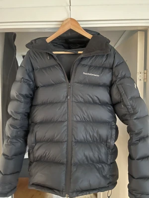 Svart dunjacka Peak Performance - Säljer en svart dunjacka från Peak Performance med klassisk puffer-look. Jackan har dragkedja framtill, hög krage och diskret logga på bröstet. Perfekt för kalla dagar och riktigt skön att bära. Passar dig som vill ha en stilren och varm jacka. Nypris 4200 kr