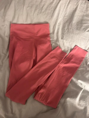 Rosa leggings från ICANIWILL - Snygga rosa leggings från ICANIWILL med hög midja och tight passform. Tillverkade i ett mjukt och stretchigt syntetmaterial som sitter skönt under träning. Diskret logga framtill i vitt. Perfekta för gymmet eller yoga.