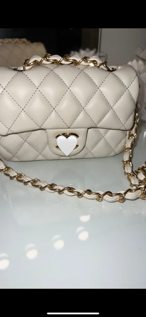 Vit quiltad axelväska med kedja - Supersnygg vit axelväska med quiltat mönster och guldfärgad kedja. Väskan har ett CC spänne framtill. Perfekt storlek för det viktigaste och ger en lyxig vibe till din outfit. HAR ANVÄNT VÄSKAN ENDAST VID ETT TILLFÄLLE 💕