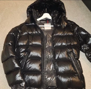Svart Moncler pufferjacka med huva - Säljer en svart pufferjacka från Moncler med glansig finish och huva. Jackan har dragkedja framtill, köpt förra vintern använd 1 gång super bra skick storleken är 2 skulle säga passar s/m