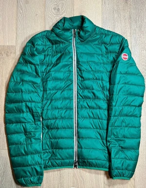 Grön pufferjacka från Colmar - Snygg grön pufferjacka från Colmar med quiltad design och markerad dragkedja framtill. Jackan har lång ärm och en hög krage som ger extra stilpoäng. Colmar-logga på vänster ärm. Perfekt för dig som vill ha en clean look med edge. Skriv om ni har frågor eller funderingar!😊