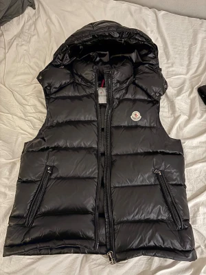 Svart dunväst från Moncler med huva - Säljer denna skit snygga moncler väst storlek L passar även M, säljs pga de vinter och för kallt för väst, defekter: litet hål långt bak i luvan man inte märker eller ser alls när man har på sig, skriv gärna dm vid intresse.