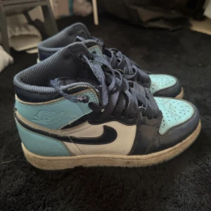 Nike Air Jordan 1 Mid Blå/Vit - Nike Air Jordan 1 Mid sneakers i blått och vitt med svarta detaljer och snörning. Skorna är lite slitna som syns på bild , och har även ett hål under sulan som också finns med på bild. Tveka inte på frågor , och pris kan alltid diskuteras! 🩵🩵