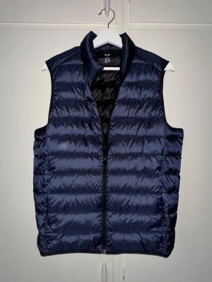 Mörkblå dunväst från Uniqlo - Säljer en mörkblå dunväst från Uniqlo (Ultra Light Down). Tillverkad i lätt polyester med dunfyllning, perfekt för lager-på-lager-stil. Strl M men passar även S