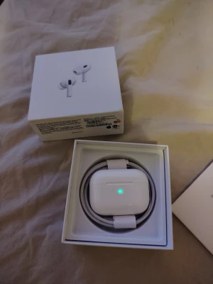 AirPods Pro gen 2 - Säljer ett par AirPods Pro i nyskick, komplett med originalkartong och laddningskabel. Laddningsfodralet fungerar perfekt och har en tydlig grön indikator. Inga synliga repor eller slitage, ser ut som nya. Perfekt för trådlös musik och samtal med aktiv brusreducering.