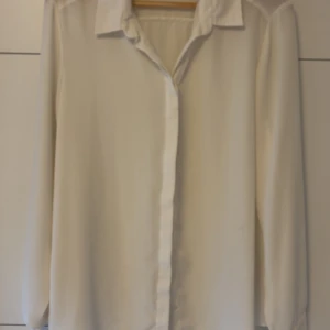 Vit skjorta från Atmosphere - Snygg vit skjorta från Atmosphere med klassisk krage och knappar framtill. Skjortan har lång ärm och är gjord i ett lätt och luftigt material som känns skönt mot huden. Perfekt för dig som gillar stilrena och enkla plagg med clean look.