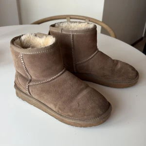 Beige ugg från Sofie Schnoor - Mysiga boots i beige mocka med rund tå och platt sula. Insidan är fodrad med mjuk, ljus päls som håller fötterna varma. Snygga sömmar och enkel design gör dem perfekta för kalla dagar. Använda en vinter, därav lågt pris! Varma och sköna