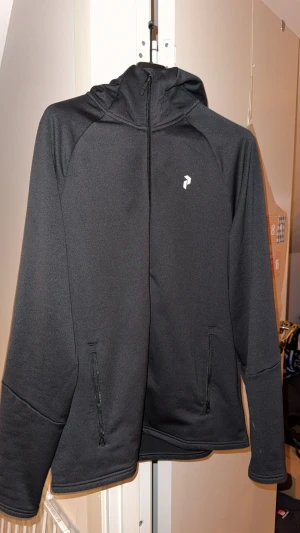Svart vindjacka Peak Performance - Svart vindjacka från Peak Performance med huva och vit logga på bröstet samt stor Peak Performance-text på ryggen. Jackan är i storlek L men kan även passa till M. Priset går att diskuteras till en vis gräns. 🙂