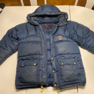 Blå fjällräven jacka - Säljer nu en fin fjälräven jacka som är i bra skick. Den har gula detaljer och guldiga knappar. Storleken är XXXL pågrund av att det är en gammal model. Men den passar S-L. Den är utsed för kvinnor men passar även fint på män. Vid snabb affär kan priset diskuteras! För mer info eller bilder är det bara att fråga!