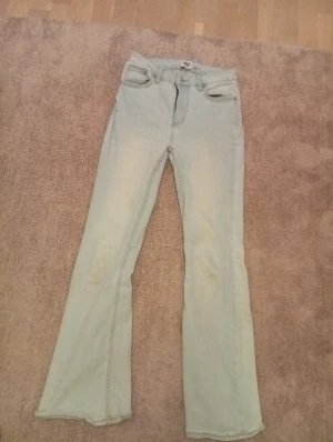 Ljusblå Snake Flare jeans från 157 storlek S-short length  - Snygga ljusblå jeans från 157 i modellen Snake Flare. Hög midja/ mid waist och utsvängda ben ger en retro och trendig look. Klassisk femficksmodell i mjukt denimtyg, perfekta till sneakers eller boots. Jeansen har dragkedja och knapp framtill. Storlek S-short length