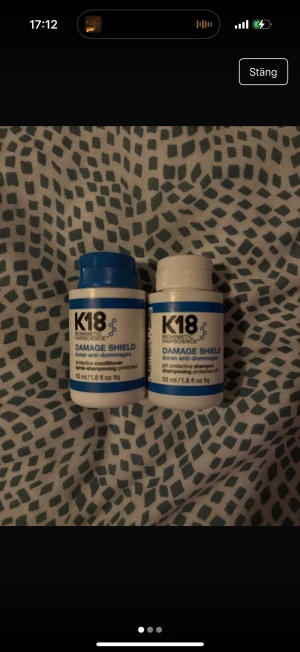 K18 Damage Shield Shampoo & Conditioner - Två flaskor K18 Damage Shield, en pH-skyddande schampo och en skyddande balsam, båda på 53 ml. Flaskorna är vita med blå detaljer och lock. Perfekt för dig som vill ge håret extra vård och skydd mot skador.