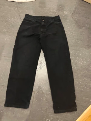 Svarta byxor från Carhartt, storlek 34 - Svarta byxor från Carhartt med klassisk femficksdesign och logopatch på bakfickan. Byxorna har rak passform