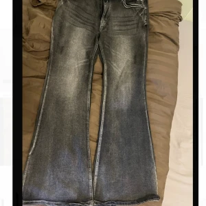 Bootcut jeans i grå tvätt - Snygga bootcut jeans i grå tvätt med slitningar. Jeansen har breda ben och en cool faded effekt framtill och baktill. Perfekt för dig som gillar retrovibbar och statement-plagg.