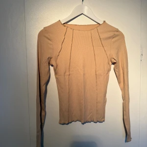 Beige ribbad långärmad topp - Säljer en beige långärmad topp med ribbad struktur och synliga sömmar framtill. 