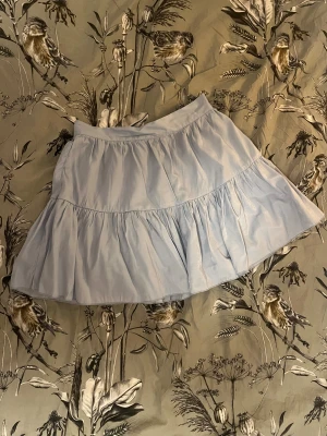 Ljusblå volangkjol från SHEIN - Supersöt ljusblå kjol från SHEIN i storlek S. Kjolen har volanger och en lätt rynkad design som ger en flowy känsla. Den är kort och har en diskret dragkedja i sidan för enkel på- och avtagning. Perfekt för dig som gillar en feminin och chill stil.