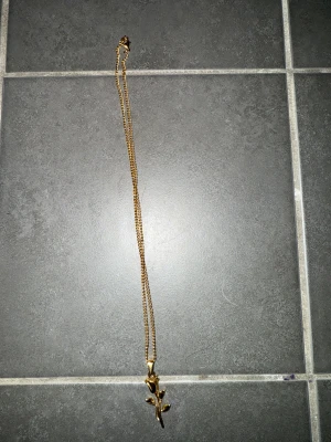 Guldigt halsband med rosberlock - Snyggt halsband plätterad med 24k guld med en detaljrik rosberlock. Kedjan är tunn och elegant, och berlocken har fina blad och en stilren blomma som hänger ned. Perfekt för dig som gillar blommiga smycken och vill ha något som sticker ut.