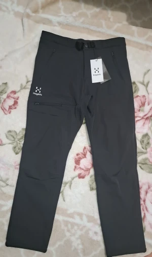 Svarta friluftsbyxor från Haglöfs - Svarta friluftsbyxor från Haglöfs med smidig passform, praktiska dragkedjefickor och justerbart bälte i midjan. Byxorna är tillverkade i slitstarkt syntetmaterial och har en stilren design med logga på benet. Perfekta för utomhusaktiviteter och äventyr.oanvänd med etikett på