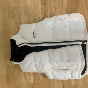 Vit dunväst från Peak Performance - Säljer en snygg och varm vit dunväst från Peak Performance. Västen har en dragkedja framtill och är perfekt för kyliga dagar. Den är i storlek S och passar bra för höst och vinter. Västen är i nyskick och har en normal passform. Perfekt för både vardag och utomhusaktiviteter!