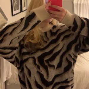 Zebramönstrad stickad tröja - Säljer en oversized stickad tröja från Part Two med beige och svarta zebraränder. Tröjan har rund hals, ribbade muddar och lång ärm. Perfekt för dig som gillar djurmönster och vill ha en mysig, cool look. Materialet är mjukt och fluffigt, passar till jeans eller skinnbyxor.