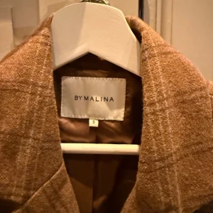 Beige rutig kappa från By Malina - Säljer en snygg beige rutig kappa från By Malina i storlek S. Den har en klassisk dubbelknäppt design. Perfekt för höst och vår, och  till vardags och fest!