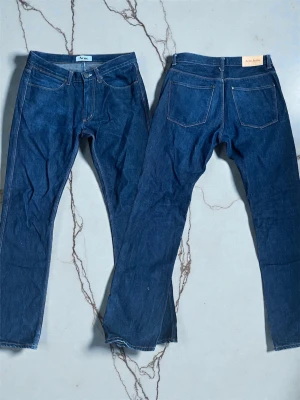 Acne Max Raw jeans blå 31/32 - Säljer ett par Acne studios jeans i klassisk mörkblå färg. Modellen har raka ben, fem fickor och orange kontrastsömmar. Jeansen är tillverkade i 100% bomull och har en stilren, tidlös look som funkar till det mesta.