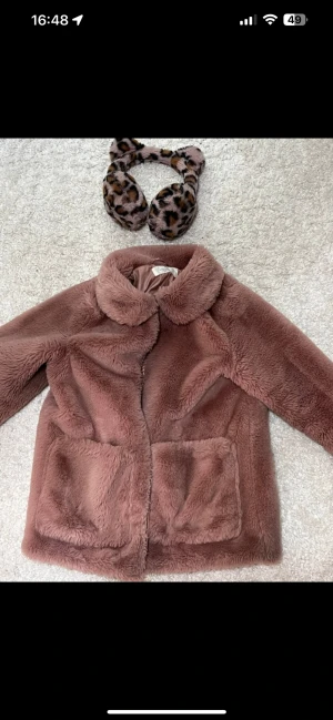 Rosa pälsjacka från H&M med dragkedja - Rosa pälsjacka från H&M med fluffigt material, stor krage och två stora fickor framtill. Jackan har en snygg guldfärgad dragkedja med ring. Kommer med leopard öronmuffar. J