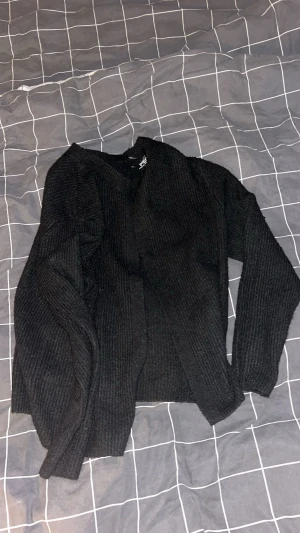 Svart ribbad kofta från pieces - Svart kofta från pieces med ribbad struktur och långärmad design. Perfekt att slänga över en t-shirt eller linne när det blir lite kyligt. Mjuk stickad känsla och enkel, klassisk look som funkar till jeans eller kjol.