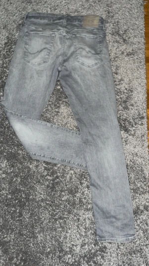Grå slim jeans från Jack & Jones - Snygga grå jeans från Jack & Jones i slim fit-modell. Jeansen har klassisk femficksdesign, diskreta slitningar och raka ben. Perfekt för dig som gillar en stilren och modern look. Materialet är mjukt och bekvämt jeans-tyg.