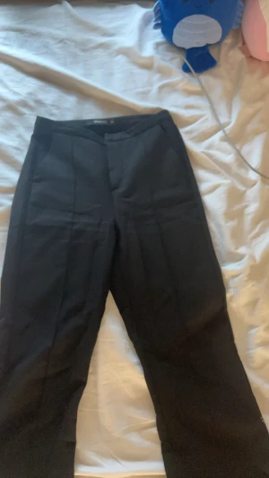 Svarta kostymbyxor Gina Tricot XS - Svarta kostymbyxor från Gina Tricot i storlek XS. Klassisk rak modell med pressveck framtill och rå kant vid benslut för en edgy vibe. Snygg midja och stilren look, perfekta till en cool outfit.