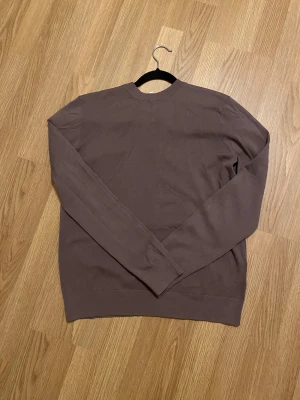 Brun långärmad tröja i bomull - En enkel och stilren brun långärmad tröja med rund hals. Tröjan är tillverkad i mjuk bomull och har en normal passform som funkar till många olika stilar. Perfekt att matcha med jeans eller chinos för en chill look.