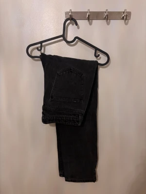 Svarta raka jeans - Säljer ett par svarta jeans med klassisk femficksdesign och rak passform. Jeansen har en enkel stil utan synliga loggor eller detaljer, vilket gör dem lättmatchade. Materialet är robust denim och färgen är helsvart.