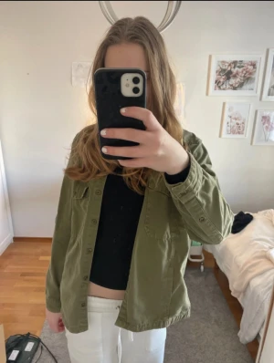 Olivgrön overshirt med fickor - Olivgrön overshirt i bomull med klassisk krage och knäppning framtill. Två bröstfickor med lock och knappar ger en chill utility-vibe. Perfekt att slänga över en t-shirt eller hoodie för en avslappnad look.