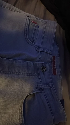Grå jeans från Prada - Snygga grå jeans från Prada med klassisk femficksdesign och exklusiva detaljer som metallmärke och logotyp på bakfickan. Jeansen har rak passform och är tillverkade i mjukt jeanstyg som ger en clean och stilren look. Perfekt för dig som gillar designerplagg.saknas ett A annars inget 