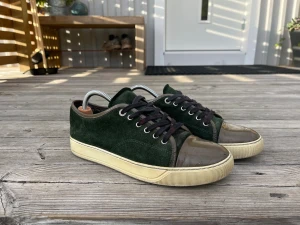 Gröna mockasneakers med lackad tå - Snygga sneakers i mörkgrön mocka med beige sula och blank, gråbrun lackad tå. Skorna har rund tå, svarta snören och metallfärgade öljetter. Perfekt för dig som gillar en unik och stilren look med coola materialmixar.