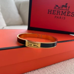 Svart och guld armband  - Stilrent armband från  i svart och guld med klassisk -detalj framtill. Armbandet har en smal, oval form och är tillverkat i metall med emalj. Perfekt accessoar för att lyfta din outfit med en lyxig touch.