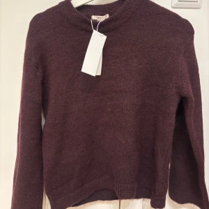 Vinröd stickad tröja Gina Tricot - Mysig vinröd stickad tröja från Gina Tricot med rund hals och långa ärmar. Materialmixen består av akryl, polyester, ull, alpacka och elastan vilket gör den både mjuk och varm. Perfekt för dig som gillar enkel och stilren design.