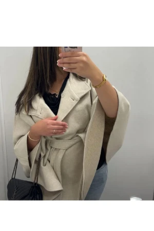 Poncho. Beige kappa med bälte och vida ärmar - Säljer en beige kappa med oversized passform, breda slag och knytskärp i midjan. Jackan har vida ärmar och en snygg, avslappnad siluett. 