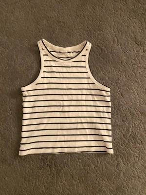 Randig linnetopp från Lindex - Säljer en vit och svart randig linnetopp från Lindex i storlek 146/152. Toppen har klassisk rak passform och ärmlös design med rund halsringning. Perfekt för varma dagar och enkel att matcha med jeans eller shorts.
