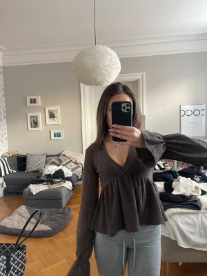 Brun omlottopp med vida ärmar - Mysig brun omlottopp med v-ringning och långa, vida ärmar. Toppen har en lätt strukturerad yta och faller snyggt över kroppen. Perfekt för dig som gillar en avslappnad men ändå trendig look.