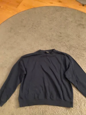 Mörkblå sweatshirt från Monki - En enkel och stilren mörkblå sweatshirt från Monki i storlek M. Tröjan har rund hals, ribbade muddar vid ärmslut och nederkant samt långärmad passform. Perfekt för chill dagar och enkel att matcha med jeans eller mjukis.