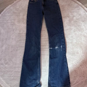 Blå bootcut jeans från Perfect Jeans - Snygga blå jeans från Perfect Jeans i klassisk bootcut-modell. Jeansen har fem fickor, dragkedja och knapp framtill samt slitning på ena benet för en cool look. Tillverkade i jeansmaterial med kontrastsömmar.