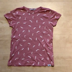 T-Shirt  - Det är en ljusrosa t-shirt med vita fjädermönster på, den är från lager 157 storlek (S barn). Den är knappt använd.