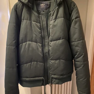 Grön vinterjacka  - Vinterjacka från Only. Mörkgrön färg, gör sig inte riktigt rättvisa på bild. Ena ”knappen” på snöret har lossnat, se bild. 