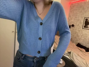 En blå kofta - Säljs på grund av att den aldrig kommer till användning. Väldigt fint skick, är en ganska kort modell, slutar vid midjan. Tröjan har en fin lite ljusare blå färg med mörkbrun spräckliga knappar.