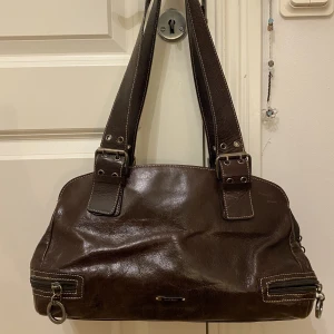 Brun väska - En brun skinnväska. Skulle säga att den är medelstor, med hyfsat korta axelband så väskan hänger vid midjan:)  150kr exklusive frakt men pris går att diskutera!☺️