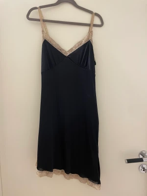 Svart siden klänning - Svart klänning i sidenaktigt material med spets! Den sitter kort och lite snedskuren med en liten slits! Kommer för sällan till användning men perfekt till fest!❤️