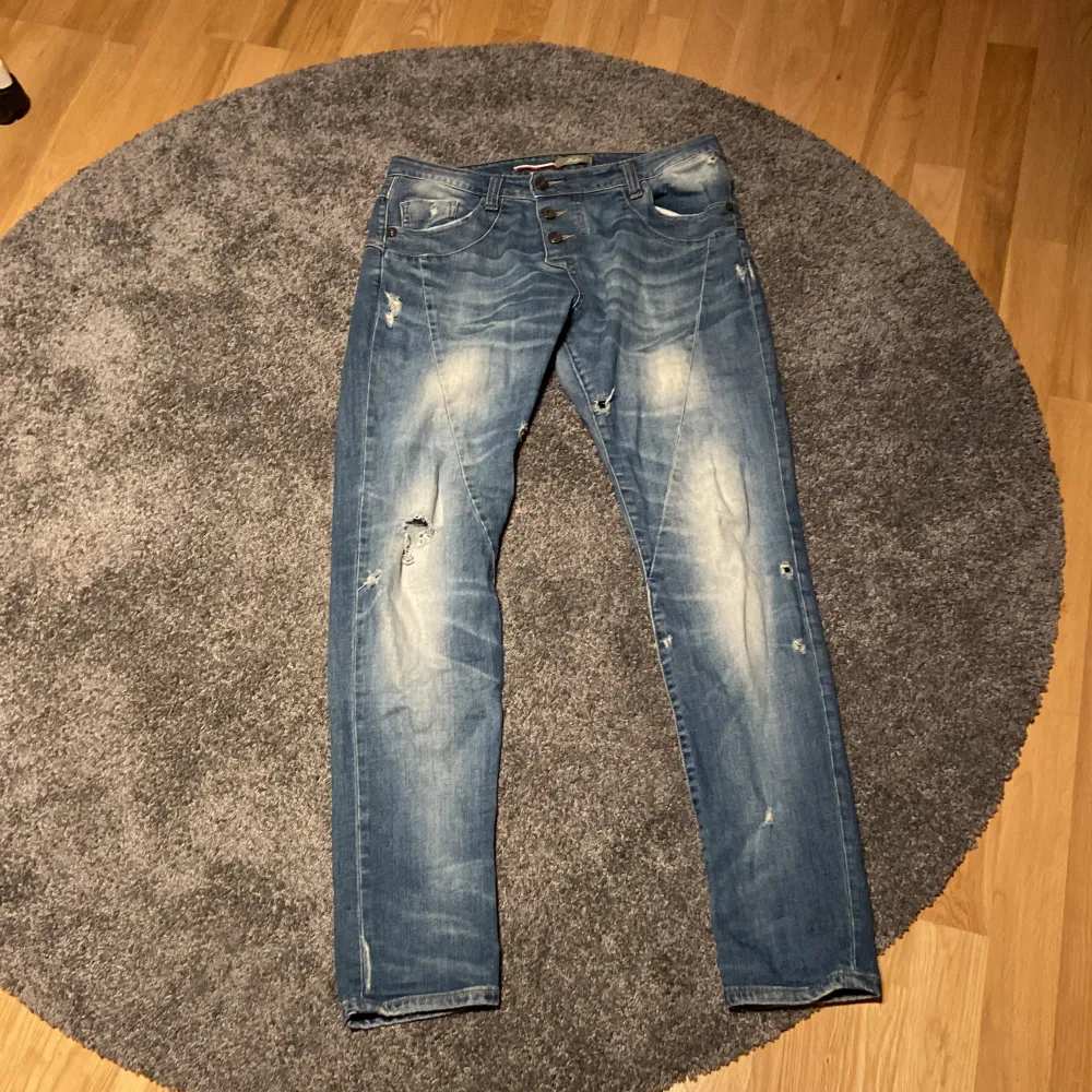 Detta är ett par blåa jeans i storlek medium.Det finns ett hjärta i silver på baksidan på höger ficka.Hålen är menade/det ska vara så. Byxorna är i  fint skick. . Jeans & Byxor.